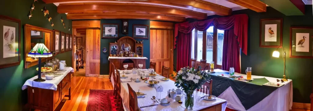A panoramic view of a vintage-style dining room with wooden walls, framed pictures, and a table set for a meal.